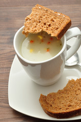 A mug of vegetable soup displayed with a broken pieces of bread