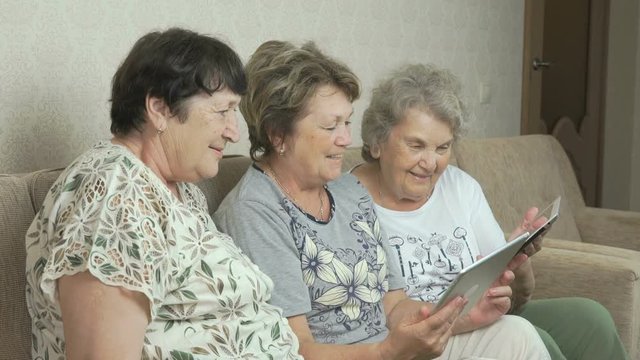 Elderly women look at photos on screen of tablets