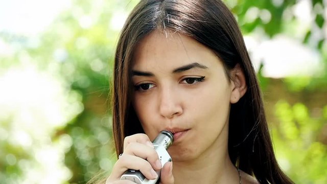 beautiful girl is vaping in green park, slow motion