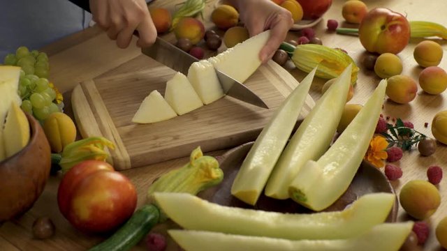 Girl sliced melon into small pieces and ate one of them. Fresh ripe melon cut into pieces. Japanese knife. Light wooden table with fruits spread out on it in the sun-drenched cuisine.