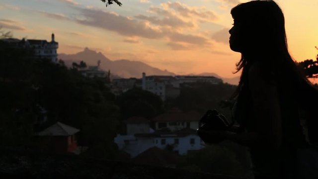 Silhouette of a woman walks into frame and takes pictures of the mountains at sunset