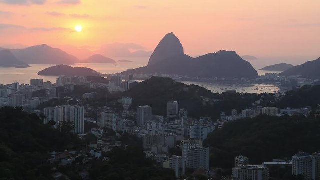 Wide shot of Sugarloaf mountain and the surrounding buildings in the city of Rio de Janeiro at sunset