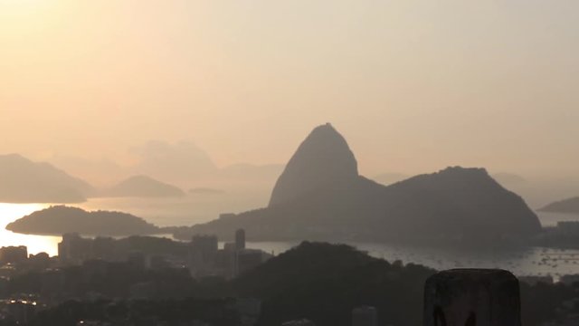 Silhouette of a woman walks into frame and takes pictures of Sugarloaf mountain at sunset