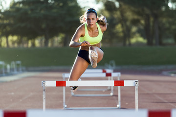 Young athlete jumping over a hurdle during training on race trac - obrazy, fototapety, plakaty