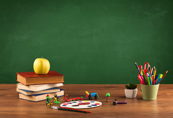 School items on desk with empty chalkboard