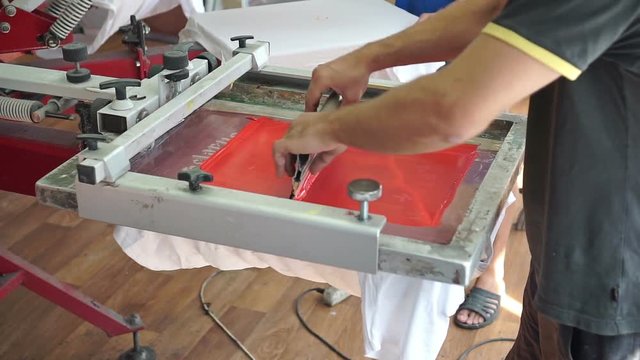 Screen printing manufacturing on t-shirts. Worker print an image on fabric on a hand bench
