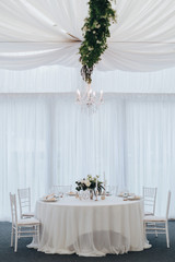 Bright tent for wedding party. Tables are decorated with white tablecloths, flower arrangements and candles