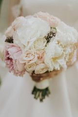 Portrait of a wedding bride posing in a white hipster style dress with flowers in her hands in the forest on sunset