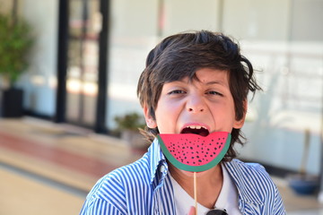 Boy pretending to eat large slice of paper watermelon