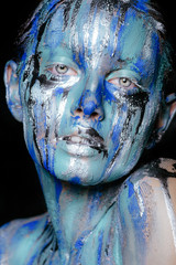 abstract art makeup. Face, neck and hair girls smeared with bright colors of blue, blue and silver colors. The paint flows. On the face of silver tears. Holi festival