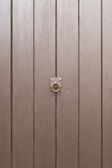 Braune Holztüre mit senkrechten Planken und Ring als Griff. Knauf in der Mitte.