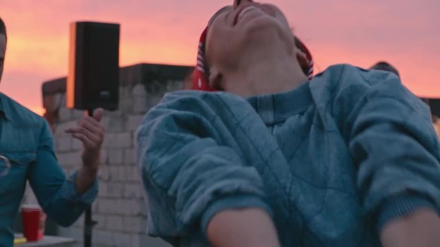 Cool curly haired girl with red bow tie headband dancing and shaking hair at sunset party on rooftop