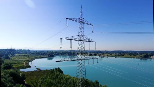 Video von einer Überland Stromleitung mit Kabeln vor einem blauen See in der Natur von unten nach oben
