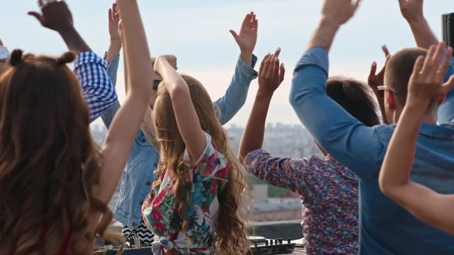 Crowd of multi-ethnic young people dancing and waving their arms in the air to the music played by dj at rooftop day party
