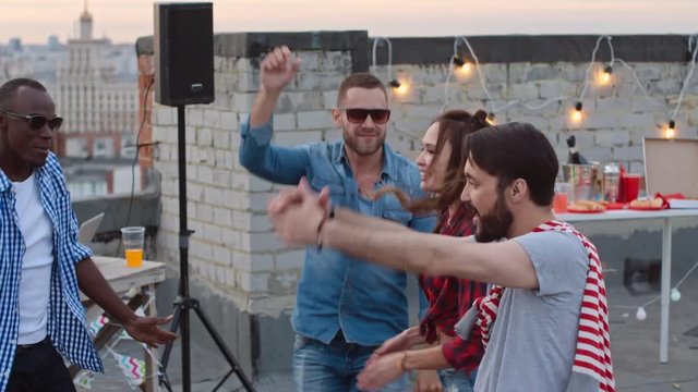 Group of carefree multi-ethnic young people dancing energetically to the music played by dj at urban day rooftop party