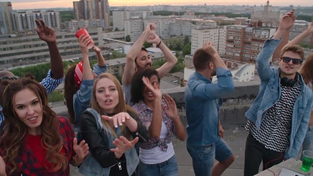 High angle view of crowd of happy multi-ethnic young people looking at camera while dancing to the music played by dj at rooftop party 