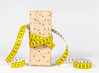 A yellow measuring tape wrapping wheat cracker or crispbread and sheaf of wheat - healthy eating...
