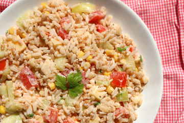 Cold salad with chicken, rice, various vegetables (tomato, pepper, cucumber, corn) and seasoning. Decorated with parsley leaves. Top view. 