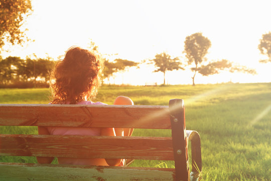 Back View Of Kid Sitting On The Bench At Sunset In The Park