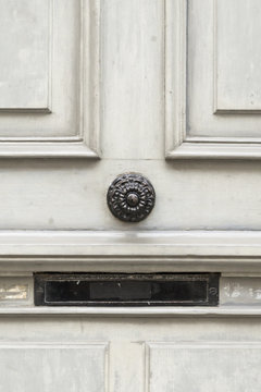 Nahaufnahme einer grau bemalten Holztür mit schwarzem Metallknauf und Briefkastenschlitz.