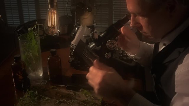 A botanist or biologist looking through an old microscope with other items in the scene that indicate the era is circa 1940. 