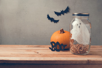 Halloween holiday decoration with ghost in jar and orange pumpkin on wooden table