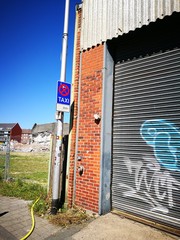 Taxistand an einer alten Fabrik mit Graffiti auf dem Rolltor bei blauem Himmel im Sonnenschein im...