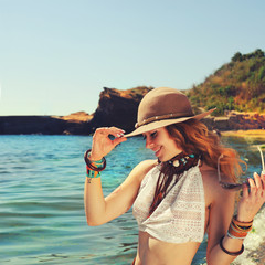 Woman traveller hiking near the sea beach, smiling and beautiful, dressed in boho chic bracelets and hat,