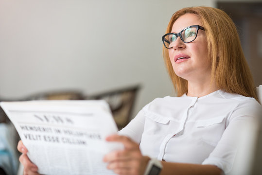 Pleasant thoughtful woman reading newspaper