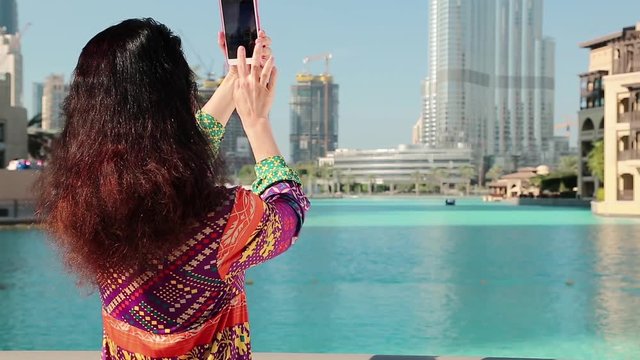 Woman stands near the blue pool and makes photos on his smartphone. Female makes photos on his smartphone. Businesswoman with smartphone. Adult woman uses his smartphone