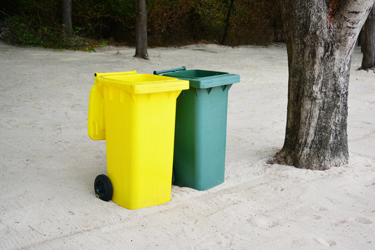 Yellow, Green bins public trash on sand.