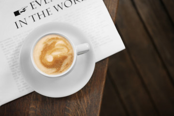 Cup of fresh coffee and morning newspaper on wooden table