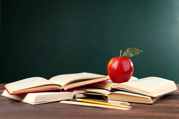 School books with stationery and apple on blackboard background