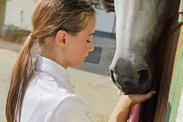jeune fille 11 ans en tenue d'équitation dans écurie, caressant cheval dans box  