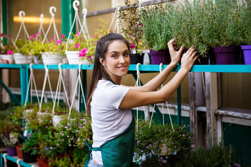 Young beautiful florist taking care of flowers over blury outdoor background.