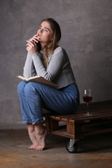 Girl sitting on board with glass of wine. Gray background