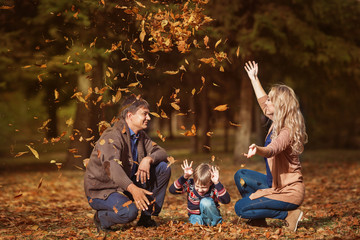 Happy smiling family throw up a leaves in a park in the autumn
