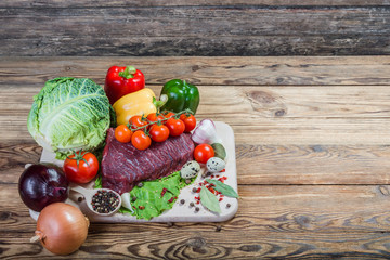 Raw meat, spices and vegetables on rustic wooden board