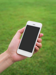 Human hand holding mobile phone against blurred green field background, Vertica