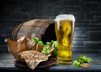 Glass of light beer with cones of hops, malt, against the backdrop of an old oak barrel