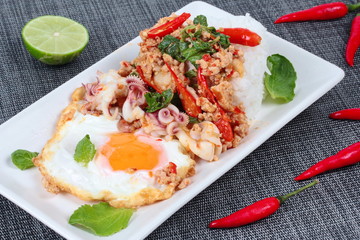 Rice topped with stirred  minced-pork ,squid ,basil and fried egg(sunny up) on black napery.