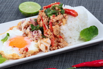 Rice topped with stirred  minced-pork ,squid ,basil and fried egg(sunny up) on black napery. Selective focus.
