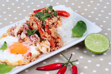 Rice topped with stirred  minced-pork ,squid ,basil and fried egg(sunny up) on brown napery. Selective focus.