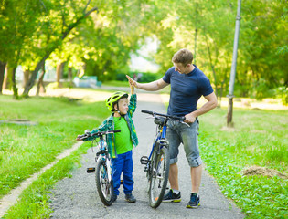 father and son give high five while cycling in the park