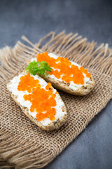 Bread with fresh cream cheese and red caviar on table.