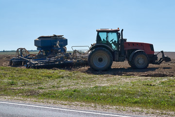 Obraz premium big red tractor with trailer seed unit of blue color is on the plowed field in the summer