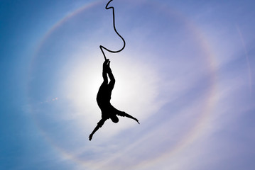 Silhouette of bungee jumper over blue sky background