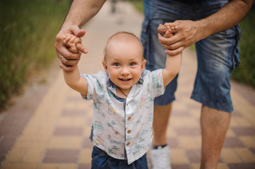Fototapeta premium Baby boy learning to walk and making his first steps holding hands of father.