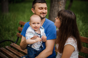 Young parents and little son in the park happy family sitting on bench