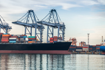 Fototapeta premium Container Cargo freight ship with working crane bridge in shipyard at dusk for Logistic Import Export background